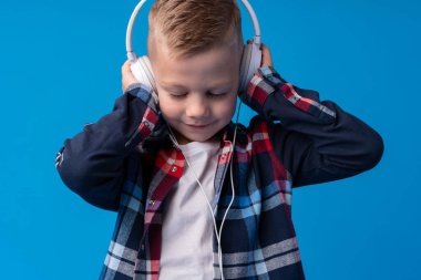 Kulaklıklı şirin bir çocuğun portresi mavi arka planda müzik dinliyor.