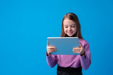 Küçük kız mavi arka planda dijital tablet kullanıyor.