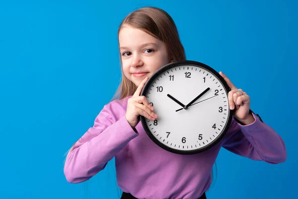 Hermosa chica adolescente sosteniendo reloj de pared sobre fondo azul — Foto de Stock