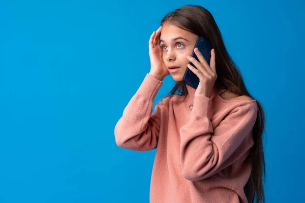 Menina adolescente bonita falando no telefone celular contra fundo azul — Fotografia de Stock