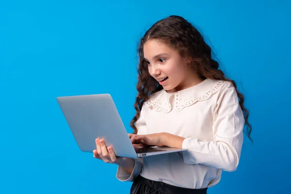 Retrato de uma menina segurando computador portátil enquanto estava contra o fundo azul — Fotografia de Stock