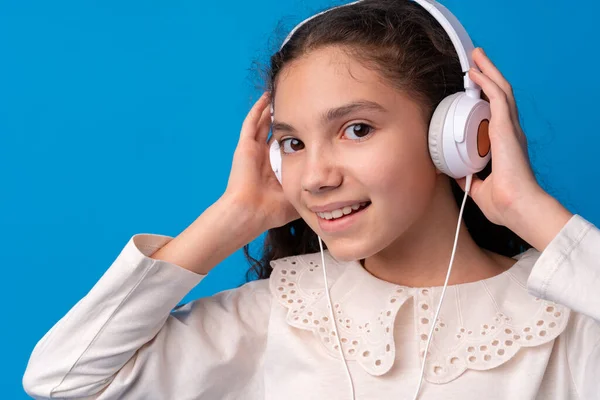 Школьница в наушниках слушает музыку на голубом фоне — стоковое фото