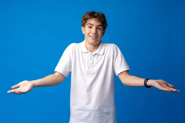 Clueless och förvirrad tonåring pojke med upphöjda armar på blå bakgrund — Stockfoto