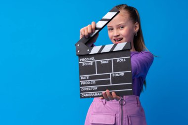 Gülümseyen kız mavi arka planda el çırpma tahtası tutuyor