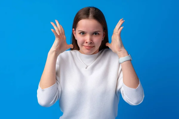 Öfkeli genç bir kadın mavi arka planda öfkeli bir şekilde el ele tutuşuyor. — Stok fotoğraf