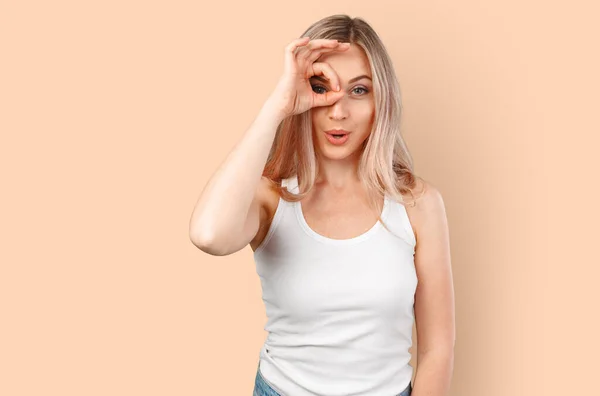 Radostné blondýny běloška žena dívá na kameru přes prsty v pořádku gesto izolované na barevném pozadí. — Stock fotografie