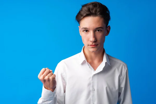 Злий стресовий хлопчик-підліток зі згорбленим кулаком на синьому фоні — стокове фото