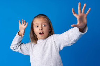 Şok olmuş küçük kız mavi arka planda şaşkınlıkla bakıyor
