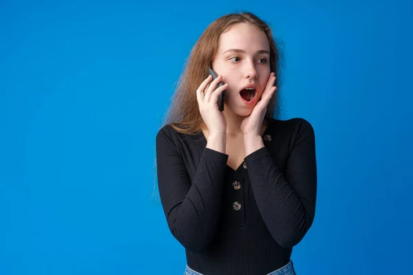 Красива дівчина-підліток розмовляє на мобільному телефоні на синьому фоні — стокове фото