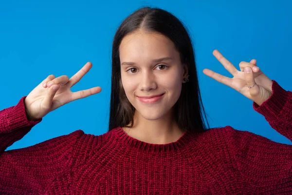 Ung tonåring flicka som visar en fred symbol med fingrar mot blå bakgrund — Stockfoto