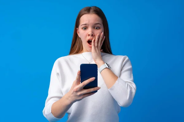 파란색 배경으로 스마트폰을 사용하는 십 대 소녀의 모습 — 스톡 사진
