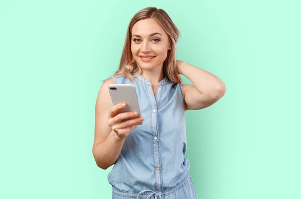 Porträt einer lächelnden, lässigen Frau, die ihr Smartphone über den farbigen Hintergrund hält — Stockfoto
