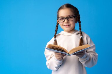 Küçük, güzel, gülümseyen kız kitabı mavi arka planda tutuyor.