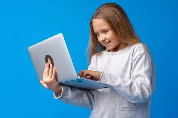 Retrato de uma menina segurando computador portátil enquanto estava contra o fundo azul — Fotografia de Stock