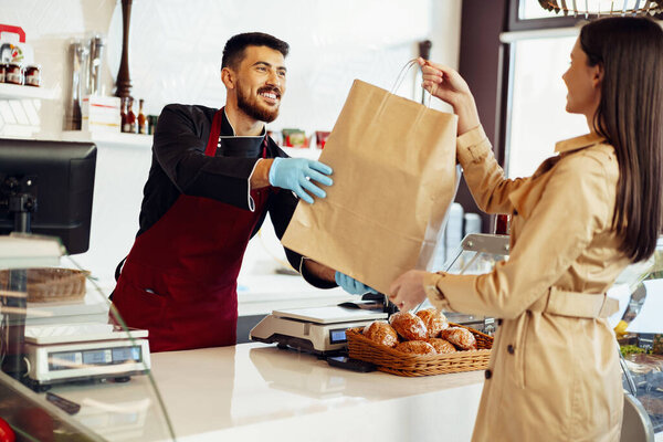 Shop assistant handling shopping bag to female customer in grocery store