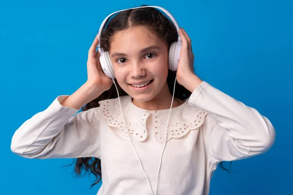 Colegiala con auriculares escuchando música sobre fondo azul — Foto de Stock