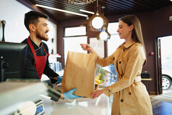 Shop assistant handling shopping bag to female customer in grocery store