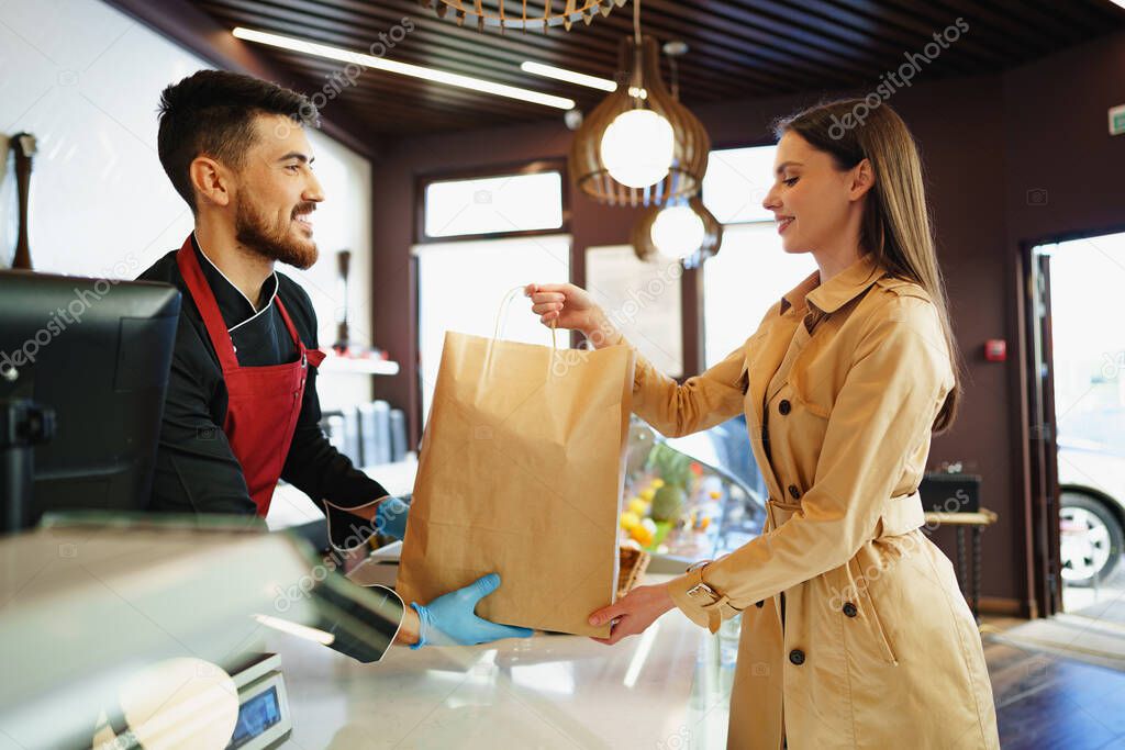 Shop assistant handling shopping bag to female customer in grocery store