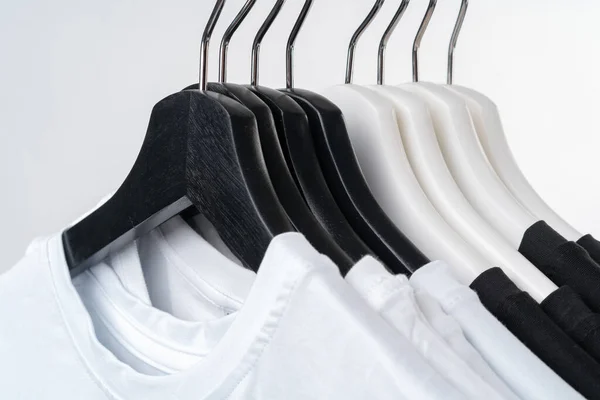 Camisetas pretas e brancas em cabides em rack de metal isolado em branco — Fotografia de Stock