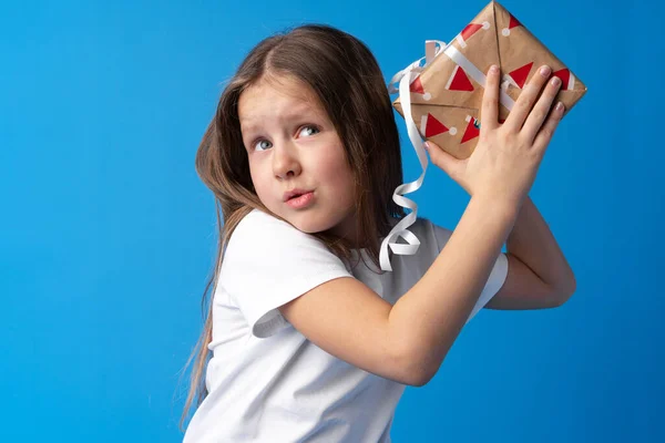 Menina feliz com cabelo comprido segurando uma caixa de presente em um fundo azul — Fotografia de Stock