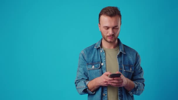 Щасливий чоловік друкує смс на синьому фоні — стокове відео
