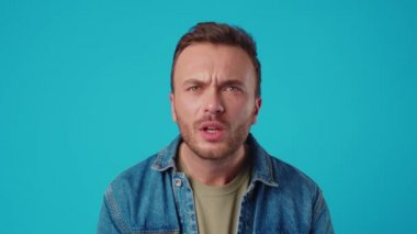 Genç yakışıklı adam mavi arka planda şaşkınlık ifadesi ve korkuyla şok oldu.