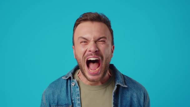 Rozzlobený mladý muž křičí na modrém pozadí — Stock video