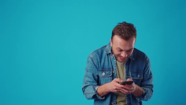 Щасливий чоловік друкує смс на синьому фоні — стокове відео