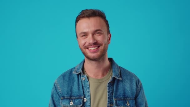 Mladý kavkazský muž se usmívá proti modrému pozadí studia — Stock video