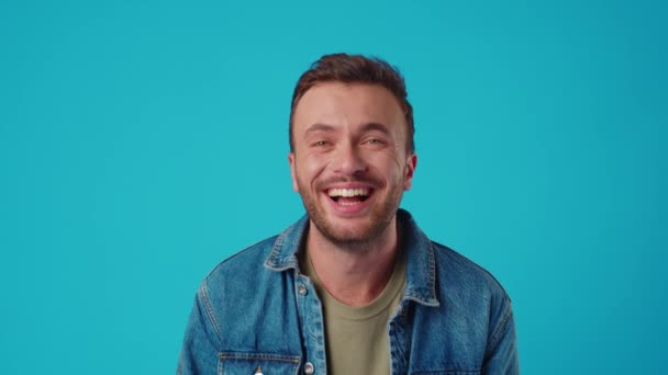 Mladý kavkazský muž se usmívá proti modrému pozadí studia — Stock video