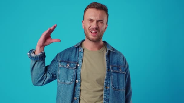 Молодой человек показывает жест бла-бла на фоне синей студии — стоковое видео