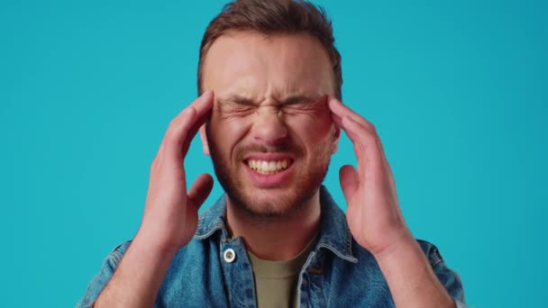 Mladý pohledný muž stojící nad izolované modré pozadí trpí bolestí hlavy — Stock video