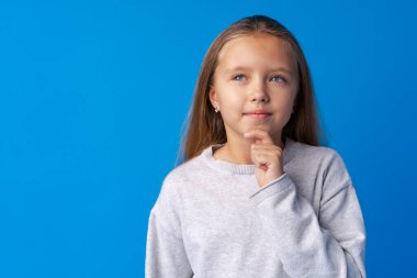 Küçük kız düşünüyor ve mavi arka plana bakıyor.