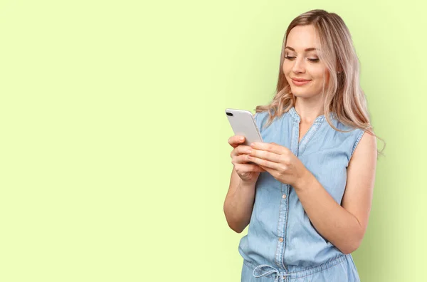 Portrait of a smiling casual woman holding smartphone over color background — Stock Photo, Image
