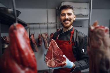 Genç kasap marketin buzdolabında çiğ et tutuyor.