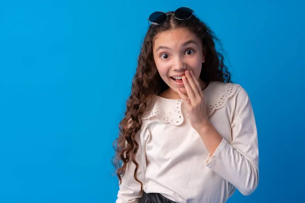 Chockad och förvånad ung tonåring flicka mot blå bakgrund — Stockfoto