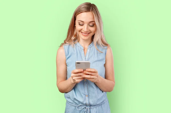Porträt einer lächelnden, lässigen Frau, die ihr Smartphone über den farbigen Hintergrund hält — Stockfoto