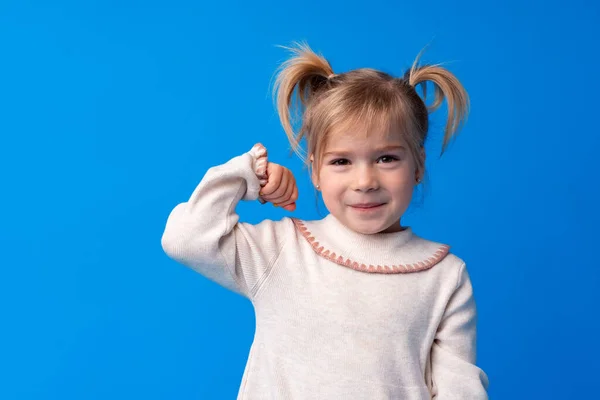 Kicsi aranyos lány mutatja erejét ellen kék háttér — Stock Fotó