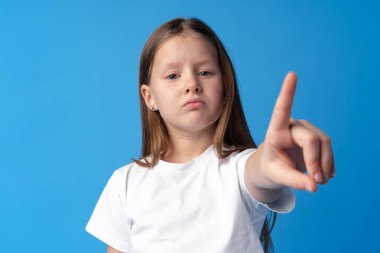 Neşeli genç kız mavi arka planda kamerayı işaret ediyor.