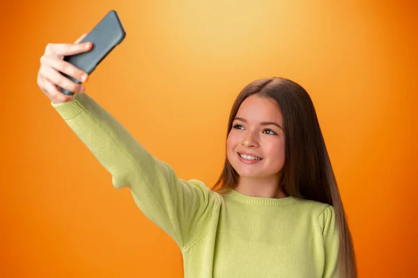 Aranyos tini lány használ mobiltelefon pozitív kifejezés narancssárga háttér — Stock Fotó