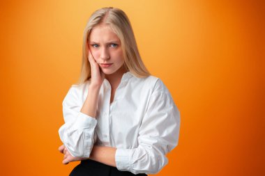 Genç kız sıkıldı ve turuncu arka plan üzerinde düşünüyor.