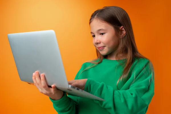 Retrato de una alegre joven adolescente sosteniendo ordenador portátil contra fondo naranja —  Fotos de Stock