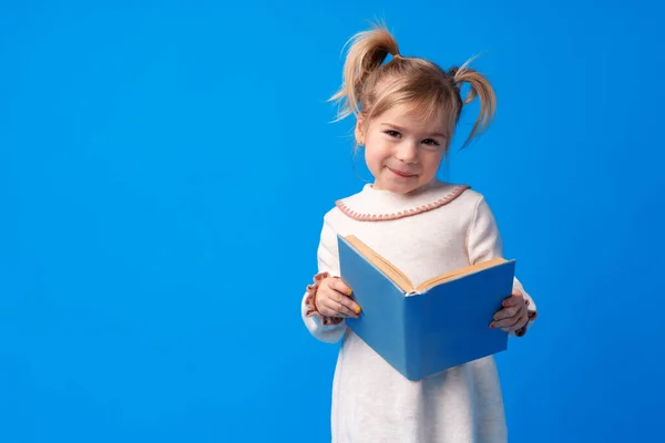 Маленькая красивая улыбающаяся девочка держит книгу на синем фоне — стоковое фото