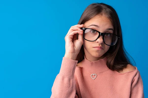 Tonårstjej justerar sina glasögon på blå bakgrund — Stockfoto