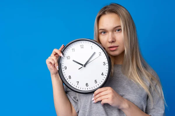 Beautiful teen girl holding wall clock over blue background — Stock Photo, Image