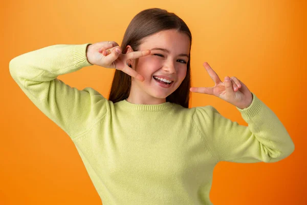 Teenagermädchen auf orangefarbenem Hintergrund zeigt Siegeszeichen — Stockfoto