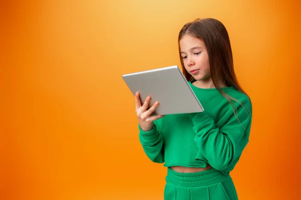 Hermosa chica adolescente usando tableta digital sobre fondo de estudio naranja —  Fotos de Stock