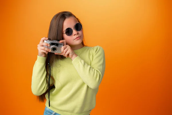 Beautiful teen girl with old photo camera against orange background — Stock Photo, Image