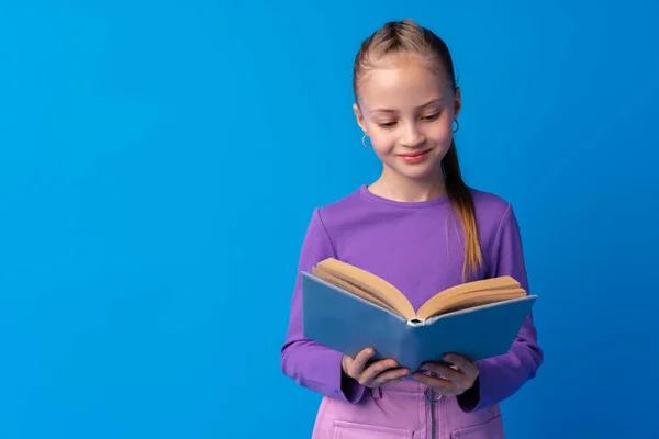 Маленькая красивая улыбающаяся девочка держит книгу на синем фоне — стоковое фото