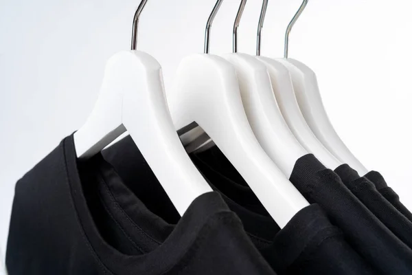 Black T-shirt on hangers on metal rack isolated on white background